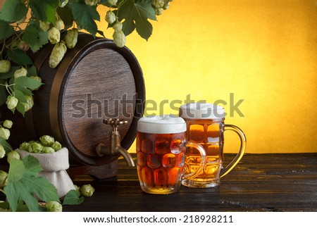 Vintage beer barrel with two beer glasses and frame of fresh hops on wooden table still life, copy space