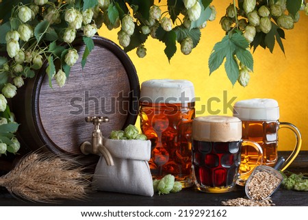 Vintage beer barrel with two beer glasses and fresh hops, metal scoop with barley on wooden table still life