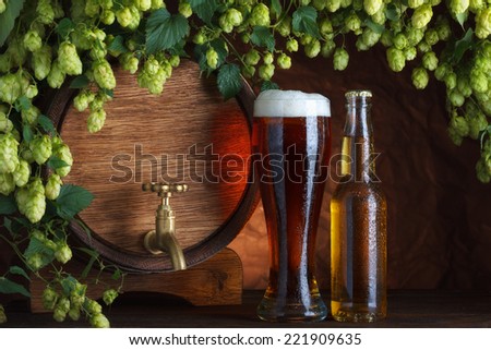 Beer glass and bottle with vintage beer barrel with fresh hops cones still-life