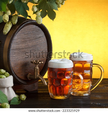 Vintage beer barrel with two beer glasses and frame of fresh hops on wooden table still life