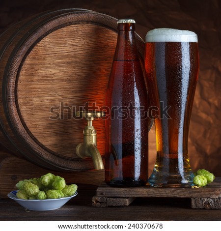 Bottled and unbottled beer glass with vintage old barrel and fresh hops for brewing still-life