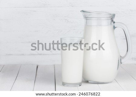 Glass of organic milk and full jar on white wooden table still life