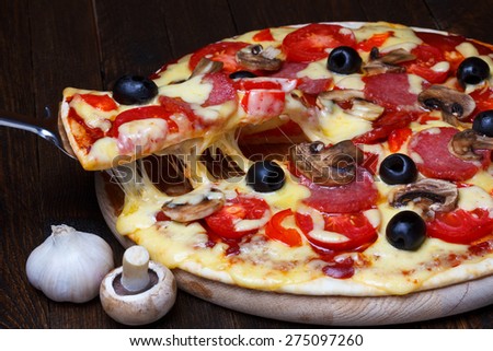 Lifted pizza slice with melting cheese on dark wooden table