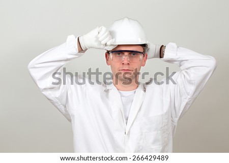 A worker is adjusting his helmet, heÃ¢Â?Â?s getting prepared to some responsible job. Direct sight. Completely white overalls, working in clean zones and rooms. Light background.