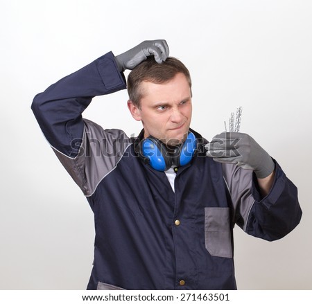 A working man in overalls makes a choice of several pieces. He puzzled scratching his head with a funny expression on his face.