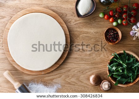 Fresh dough pizza base  and ingredients on a wooden textured table. Top view.