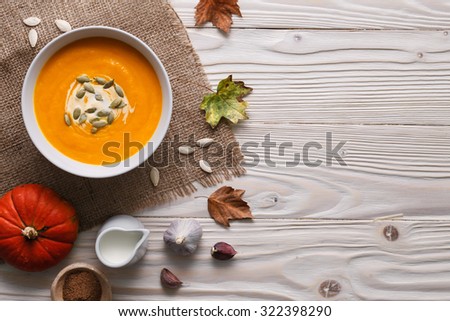 Traditional pumpkin soup with seeds and fresh just baked rye bans on a white wooden background.