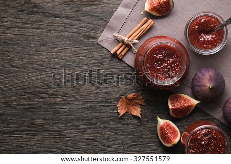 Glass jars full of fig jam and fig fruits on a dark wooden background