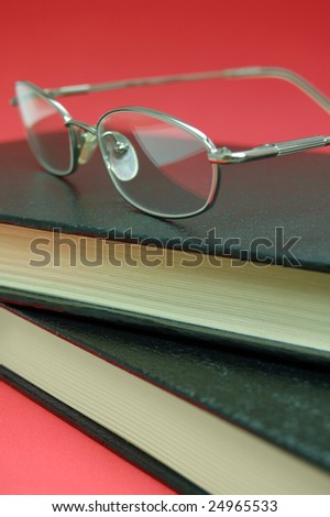 Silver eyeglasses on top of two books on red background