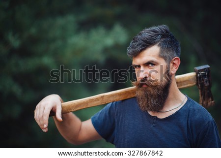 brutal brunette bearded man with a hatchet in the woods on a background of trees