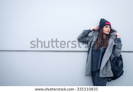 young woman with long hair, with a leather backpack, a warm hat, beautiful makeup, leather pants, a gray sweatshirt and a leather shirt, high heels walking one in the production hall and the street