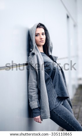 young woman with long hair, with a leather backpack, a warm hat, beautiful makeup, leather pants, a gray sweatshirt and a leather shirt, high heels walking one in the production hall and the street