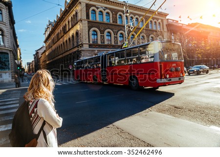 unknown girl with a backpack at the intersection waiting to cross the road and looking at a passing trolleybus, Hungary, Budapest, autumn 2015.