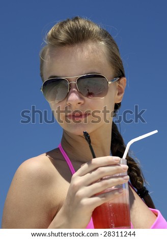 The young woman with juice on a beach against the blue sky