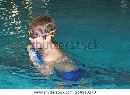 A little boy swims in a pool. A boy with glasses for swimming and equipment. Sports concept.