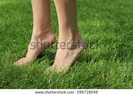 A pair of women\'s feet on the green grass.  Legs crossed each other. Legs in focus from the side pictures. Nature, lawn, yard