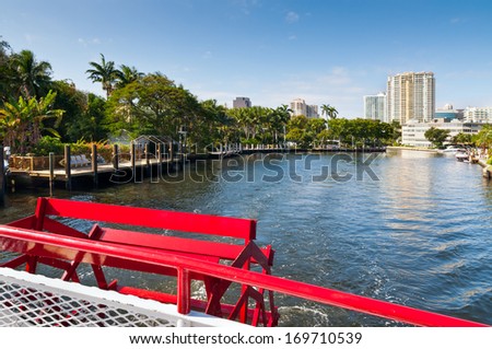 Boats traverse the inland waterways of Fort Lauderdale, Florida. Tall buildings, luxury houses and trees frame the canal.