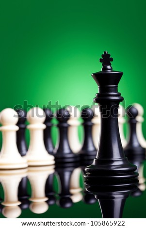 black king standing in front of all the pawns, black and white, on green background - closeup picture