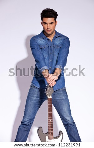 young fashion guitarist holding his guitar on the floor while looking to the camera and posing