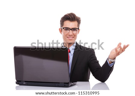 young business man welcoming you at his desk with laptop isolated on white