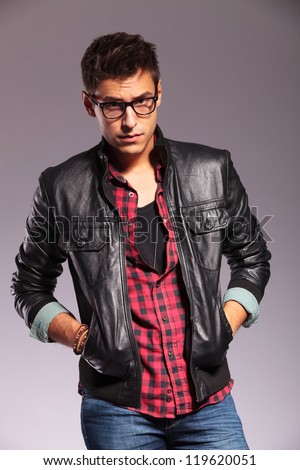 young casual man wearing glasses and leather jacket standing with hands in pockets