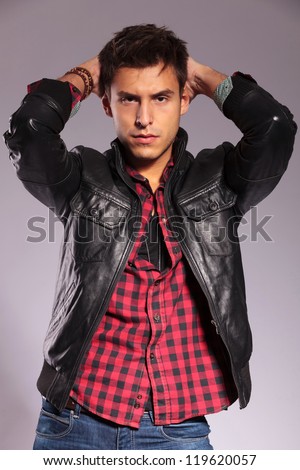 young casual man in leather jacket in a fashion pose with hands on his head