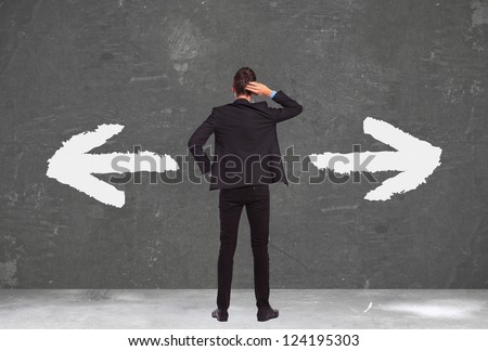 back of an undecided young business man standing with his hand on his head and thinking waht to do