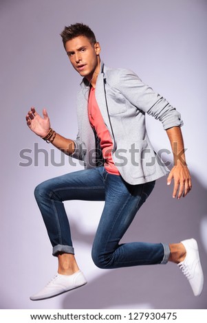young man jumping in the air in a running position, looking at the camera, over light background
