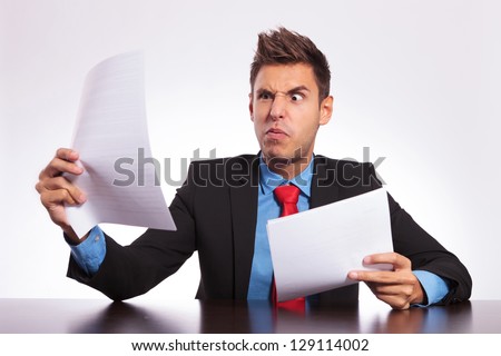 young business man at the table reading something unbelievable and making a weird face