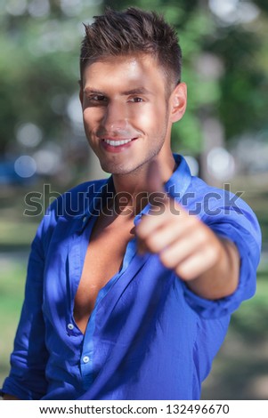portrait of a young casual man in the park showing thumbs up gesture with a smile on his face