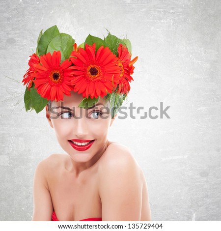 young  woman with red gerbera flowers on her head  looking to her side, on a gray background