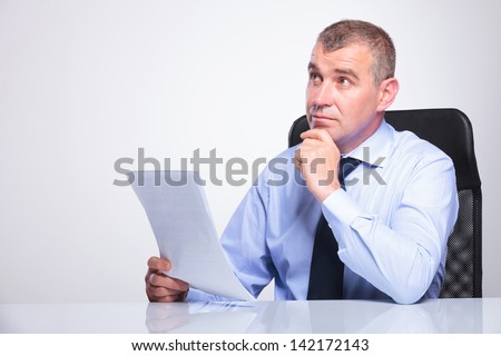 senior business man sitting pensive at his desk with some documents in his hands, looking away from the camera. on gray background