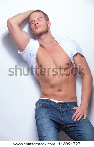 young fashion man with t-shirt pulled over his neck holds his hair back and his eyes closed. on light gray background