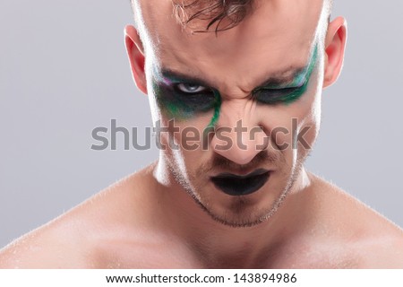 closeup of a casual young man with dramatic makeup looking at the camera with one eye. on gray background