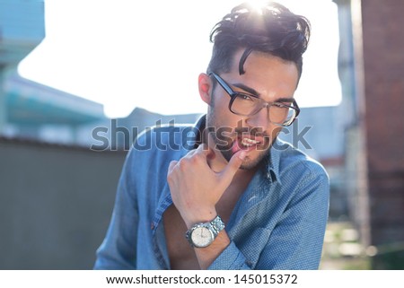 casual young man posing outdoor with a hand on his lower lip while looking at the camera