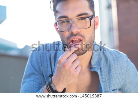 sensual casual young man outdoor touching his lower lip while looking at the camera