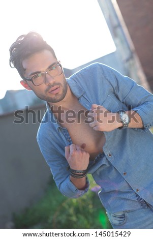 casual young man outdoor taking off his shirt while looking at the camera