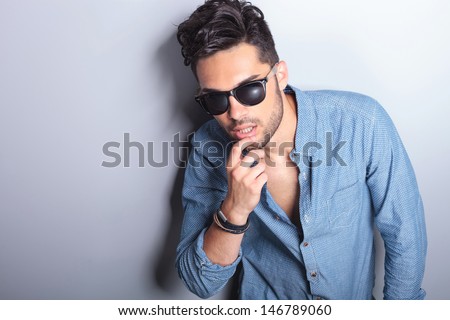 sensual casual young man touching his lower lip while looking at the camera. on gray background