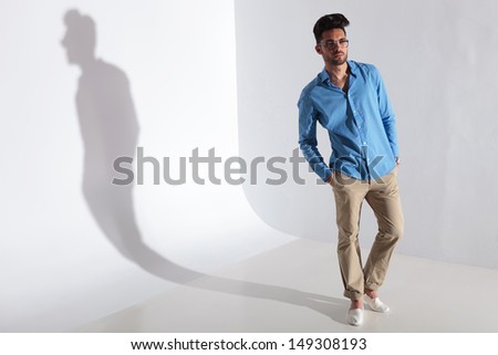 full length picture of casual young man standing with his hands in his pockets. on light gray background with shadow