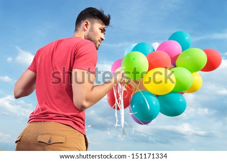 back view of a casual young man holding balloons outdoor and looking to his side