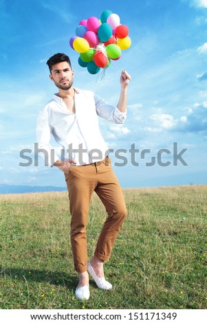 full length picture of a casual young man holding balloons outdoor and a hand in his pocket