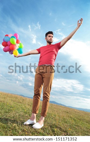 casual young man outdoor creating the illusion of holding a bunch of balloons in his hand