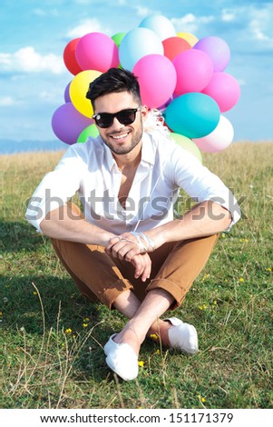 seated casual young man holding balloons outdoor and smiling for the camera