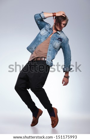 full length portrait of a casual young man balancing on his toes while holding his cap and looking to his back, away from the camera. on gray studio background