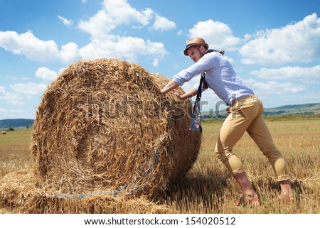 full length photo of a young casual man pushing a big haystack and looking away