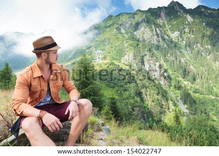 seated young casual man outdoor looking back at the beautiful mountain behind him
