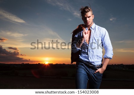 casual young man standing with a hand in his pocket outdoor during sunset