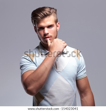 sensual young casual man touching his lower lip while looking into the camera. on gray background