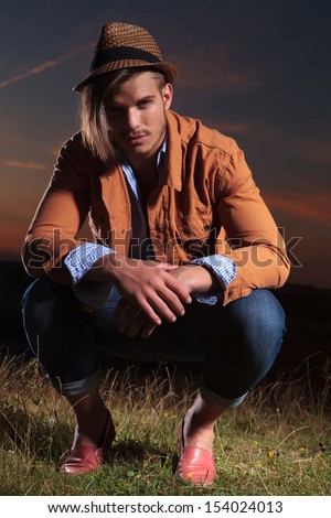 casual young man sitting crouched outdoor and looking into the camera