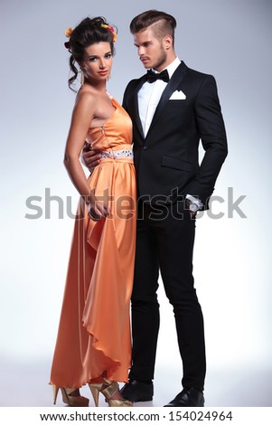 full length portrait of a young fashion couple with man holding and looking at woman while she is looking at the camera. on gray background